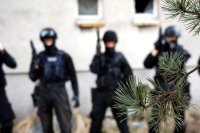 zbliżenie na gałąź drzewa iglastego. w tle 4 policjantów gsr z bronią
