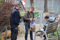 policjantka pracownik ops i strażnik wręczają paczkę bezdomnej na ławce w parku