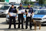trzej policjanci którzy zwyciężyli trzymają puchary obok stoi pies