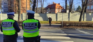 Policjanci obserwują mężczyznę, który zbliża się do przejścia dla pieszych i korzysta z telefonu.